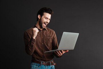 Delighted handsome guy making winner gesture and using laptop