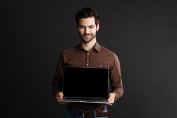Joyful handsome brunette guy smiling while showing laptop