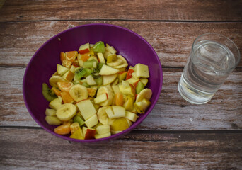 Fruit salad in a bowl with glass of water on wooden background