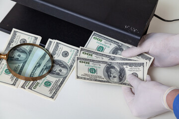 Gloved hands checking dollar bills on detector