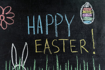 Happy Easter on chalk board, egg and spring flower, grass and easter bunny ears.