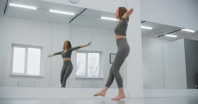 Dancer woman jumps in slow motion infront of mirror wall, gymnastics in the white dance hall, stretching trainer, yoga instructor, 4k 120p Prores HQ