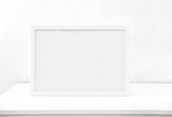 Horisontal White frame mockup  on a white table against white  wall. Empty poster frame mockup for design. Copy space