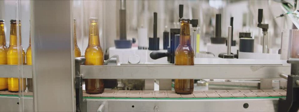 Full beer bottles moving along the factory line in a brewery. Bottle labeling machine in a brewery. Modern technology machines in a factory. Factory, brewery concept.