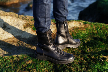 Blue jeans and black boots in eco leather on laces for active tourism in the forest or mountains on a green background