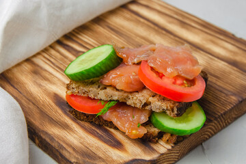 Red fish sandwich with wholegrain bread, cucumber, and tomatoes laying on a wooden board