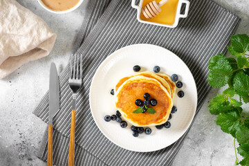 Pancakes in a white plate on the light gray kitchen table. Homemade delicious pancakes with honey and blueberries. Delicious sweet and hearty breakfast