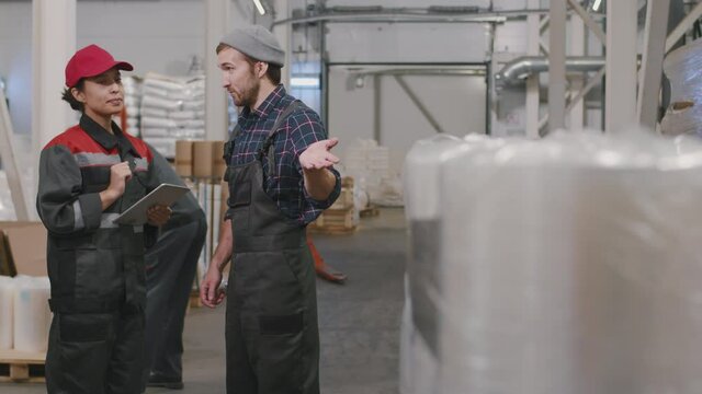 Medium slow-motion footage of multi-ethnic plant workers talking at polyethylene production factory with piles of transparent plastic film everywhere
