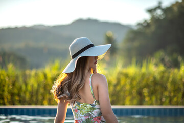 Burry image a young Asian woman with long hair wearing a white straw hat. She is moving and relaxing in a warm summer swimming pool on a sunny day. Tropical summer vacation and holiday concept