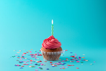 Pink birthday cupcake with green candle and confetti on blue background