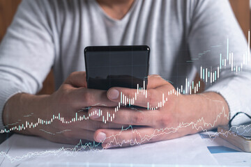 Trader holding in the hands a smart phone and researching stock market to proceed right investment solutions. Internet trading and wealth management concept. Hologram Forex chart over close up shot.