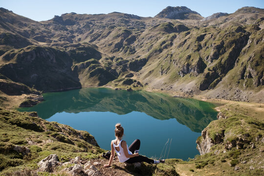 Young woman sitting alone on the ground in front of the beautiful mountain lake, watching the landscape of Somiedo natural park, blue calm surface,