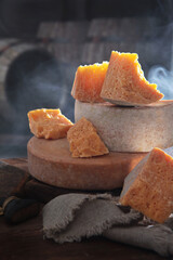 Chunks of hard aged cheese on the background of barrels. Light smoke in the background. Long-term cheese. Vertical photo.