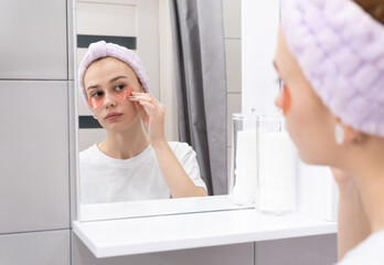 Skin care concept. Young girl puts patches on her face in front of the bathroom mirror