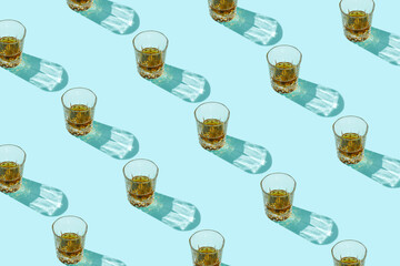 Pattern made of drink, glasses and beverage with trend shadows on blue background. Beautiful reflections from glass on backdrop. Minimal summer refreshment or alcohol layout. Flat lay.