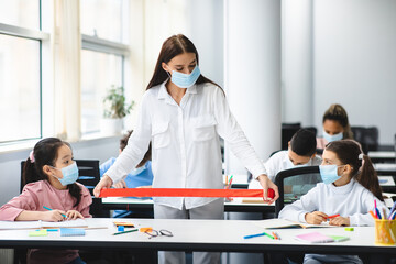 Fototapeta premium Teacher in face mask using red tape measuring social distancing