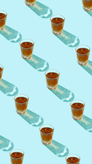 Pattern made of drink, glasses and beverage with trend shadows on blue background. Beautiful reflections from glass on backdrop. Minimal summer refreshment or alcohol layout. Flat lay.