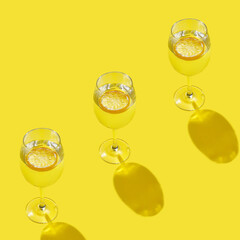 Summer stationery still life scene made with three glasses in row and trend shadow on trend yellow background. Summer vacation refreshment concept. Long shadow and refraction pattern.