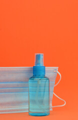 Hygienic and health measures. Hand sanitizer gel and surgical mask on orange background.