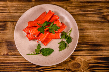 Ceramic plate with pile of crab sticks and parsley twig on a wooden table. Top view