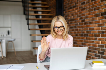 A charming blonde mid age women has video conference on the laptop, an office female employee...