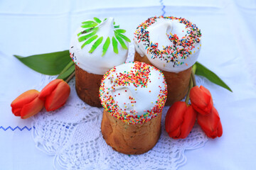 Three beautiful Easter cupcakes with colorful decor and five red tulips on a white lace tablecloth