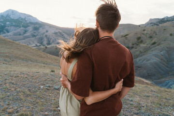 Lovers enjoy the sunset. The guy and the girl are standing and hugging. Romantic date at the top of the mountain. Valentine's Day is celebrated by lovers