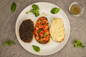 Bruschetta with tomato sauce, bruschetta with black olive cream and bruschetta with artichoke cream on the plate. Mix of Italian bruschetta. Classic Italian appetizer. Flat lay.