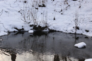 
Snow lies on the banks of the river. The tree and the sun are reflected in the water. Water turns to ice
