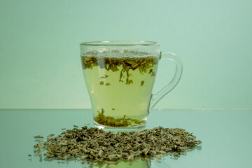 A cup of green tea is on the table. Dry green tea leaves are scattered nearby. Green tea. Transparent cup. Advertising, copy space.