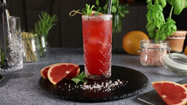 Pink Grapefruit Mezcal Paloma Cocktail in highball glass with water drops on table in real home. New life concept of quarantine. Camera moving, close up, shallow depth of the field.