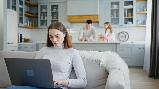 Business during covid-19 pandemic. Confident woman working on laptop while husband playing with kids on background