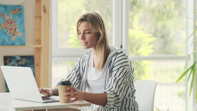 A beautiful young woman is using her laptop computer sitting at the table in the art studio