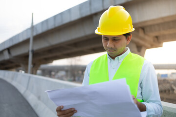 Young asian engineer reading a drawing at construction site