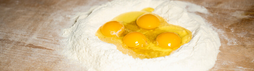 (Selective focus) Close-up view of a heap of flour with some fresh eggs inside. Flat lay, Ingredients for a homemade dough such as pasta, bakery, cakes etc.
