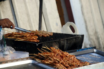 Pork on bamboo skewer are grilling on black grate, Thai street food. Blur hand is clamping raw pork on grate.