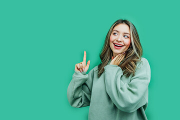 On a green background smiling beautiful girl shows a thumb up where is the place for text. Commerce. Photo for advertising. Discounts. Online shopping