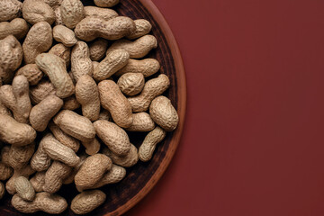 Unpeeled peanuts in a clay plate on a brown background