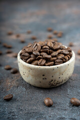 Roasted coffee beans in a ceramic bowl selective focus. Scattered coffee beans on background. High quality photo. Close up. Macro.