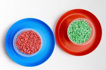 Colorful decorative natural stones in plastic containers on red plastic plate on a white background