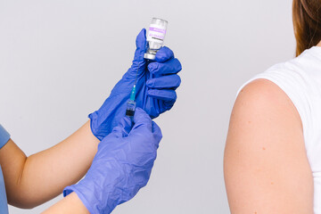 Cropped photo. The hands of a medic in protective gloves with a syringe and ampoule prepare a covid 19 vaccine for a patient. Grey background. Fighting the spread of the virus.