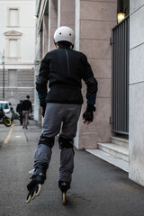 A man wearing helmet and knee pads on roller skates riding outdoors on urban street