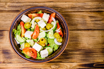 Ceramic plate with greek salad on wooden table. Top view
