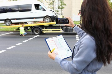 Woman with documents in hands taking pictures of wrecked car on phone. Car insurance concept