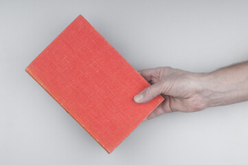 Hand holding book with red cover on gray background