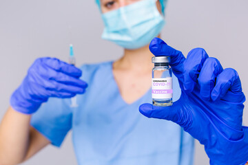 Blurred photo of a healthcare professional worker with syringe and ampoule of covid 19 vaccine on a gray background.