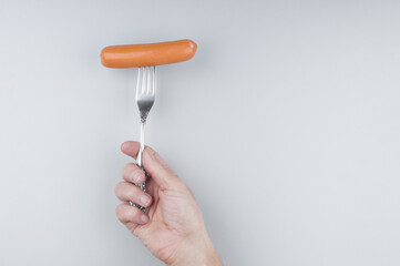 Hand holding fork with sausage on gray background