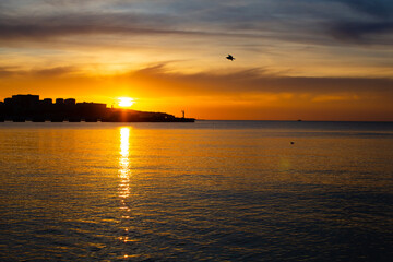 The sun is setting at sunset behind the houses on the sea