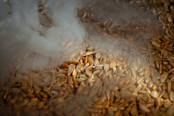 Peeled sunflower seeds close up. Seed texture. Lots of seeds in a pile. Contrasting dramatic light as an artistic effect. Smoke and steam from roasting seeds in the background.