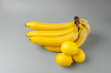 Bunch of bananas and three lemon on a gray background. Trending color Pantone of year 2021 Illuminating and Ultimate gray. Side view minimal still life.